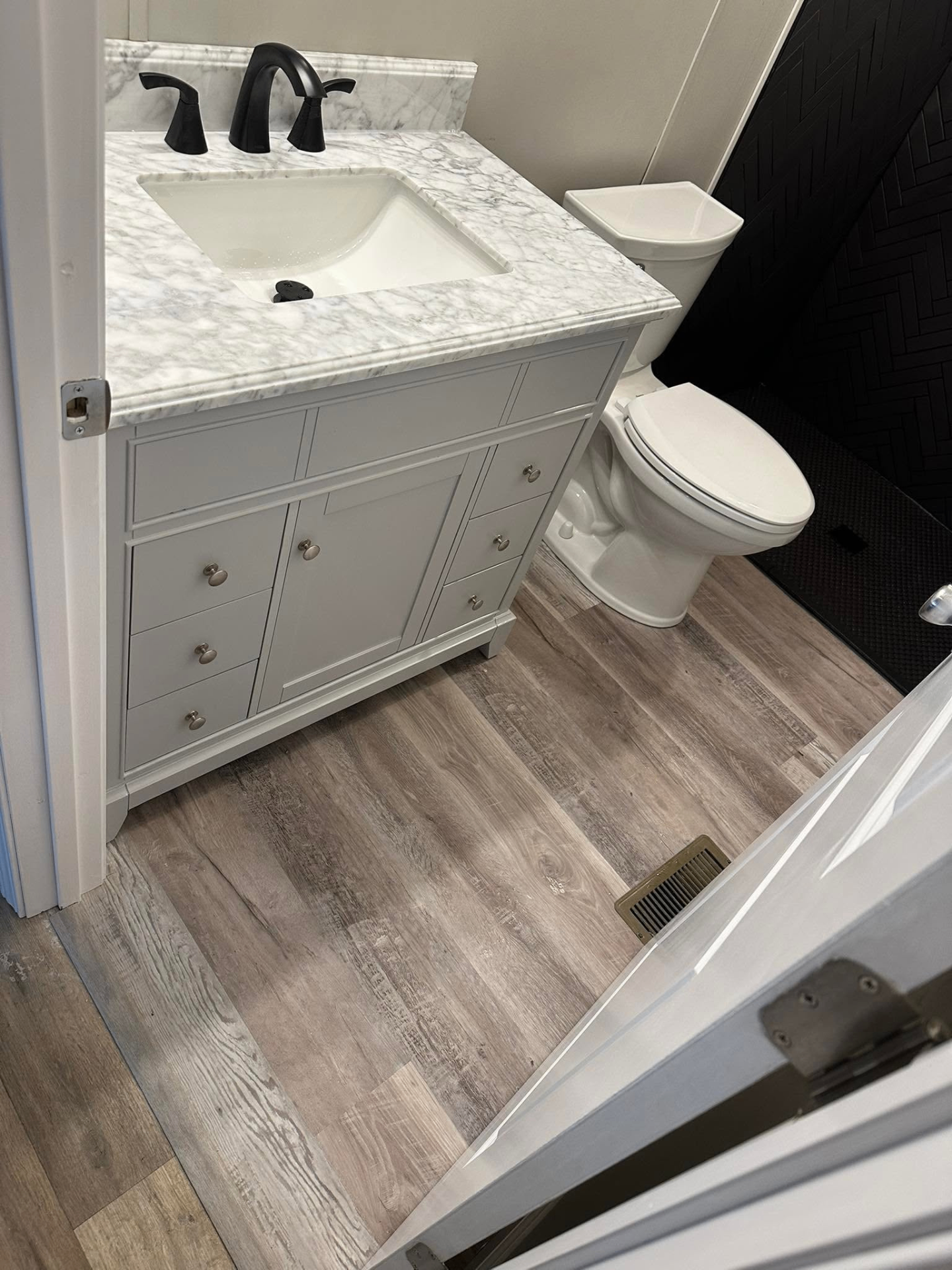Renovated bathroom with gray shaker vanity, marble countertop, matte black faucet, and wood-look plank flooring